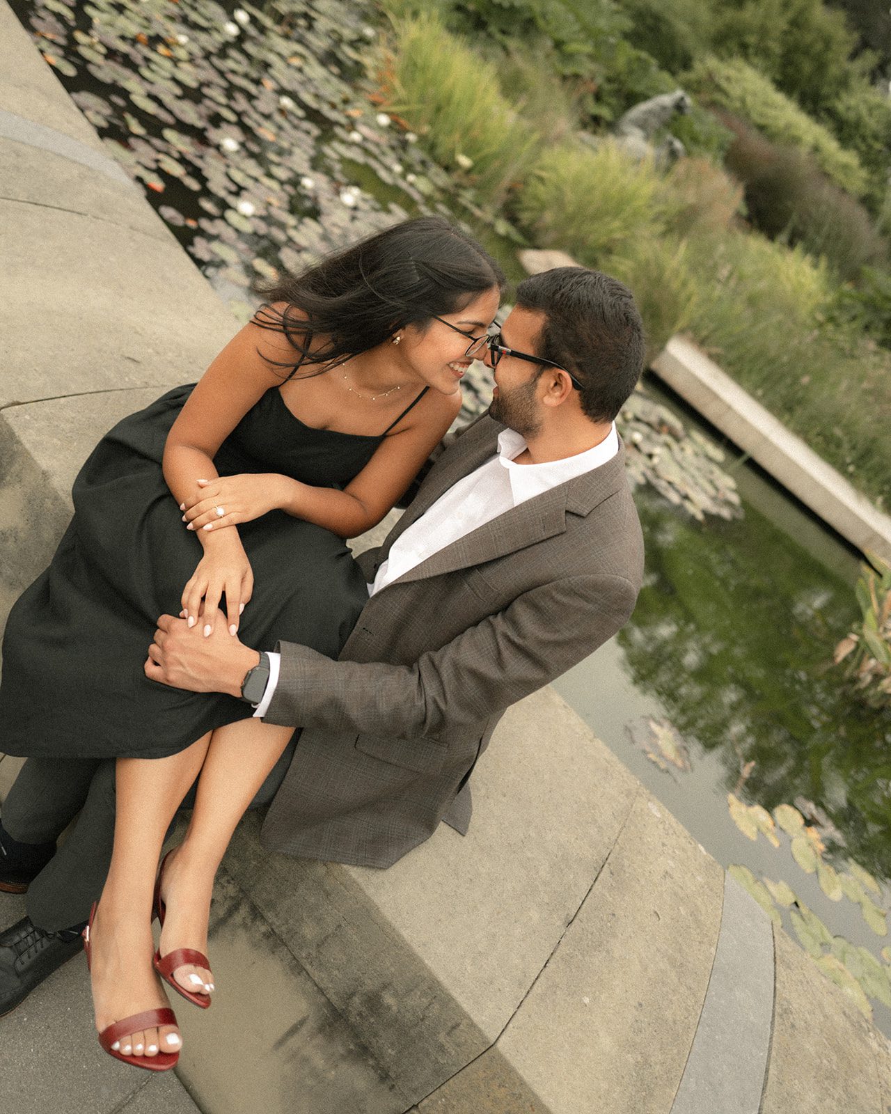 Couple sitting closely beside a lily pond in formal engagement photo outfits, sharing a candid moment during their San Francisco Engagement Photos.