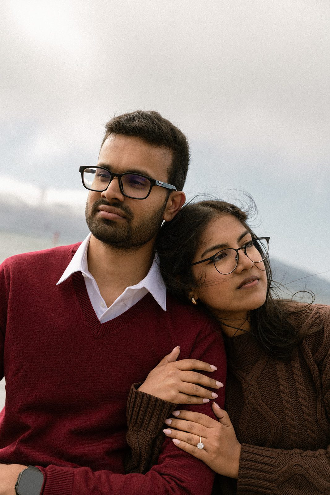 Close-up of a couple leaning together in coordinated burgundy and brown sweaters, with the engagement ring visible during their San Francisco engagement session.