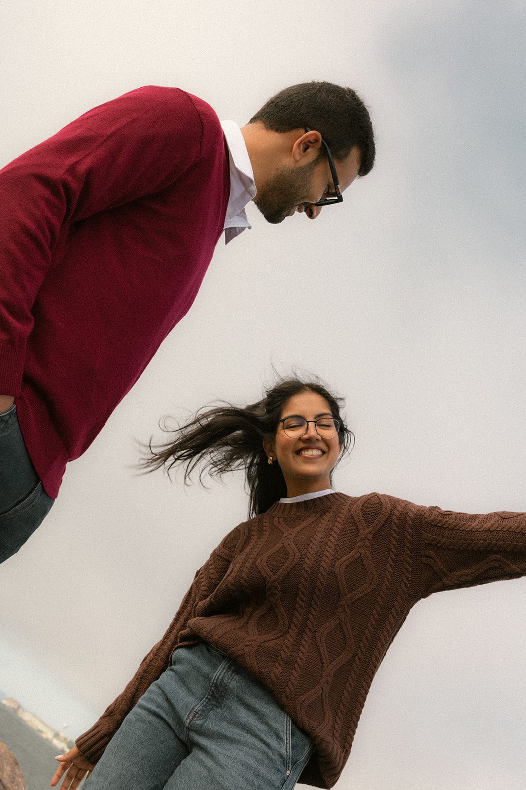 Low-angle candid of a couple laughing in brown and burgundy sweaters, a playful approach to casual engagement photography during their San Francisco engagement session.