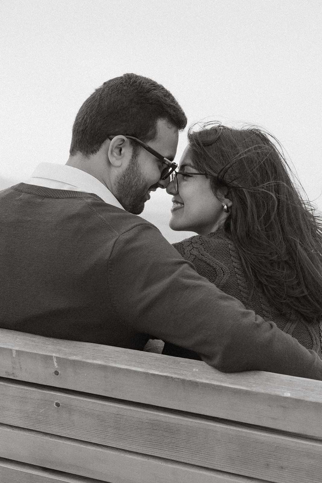 Black-and-white close-up of a couple touching foreheads on a bench, capturing a candid moment during their San Francisco engagement session.
