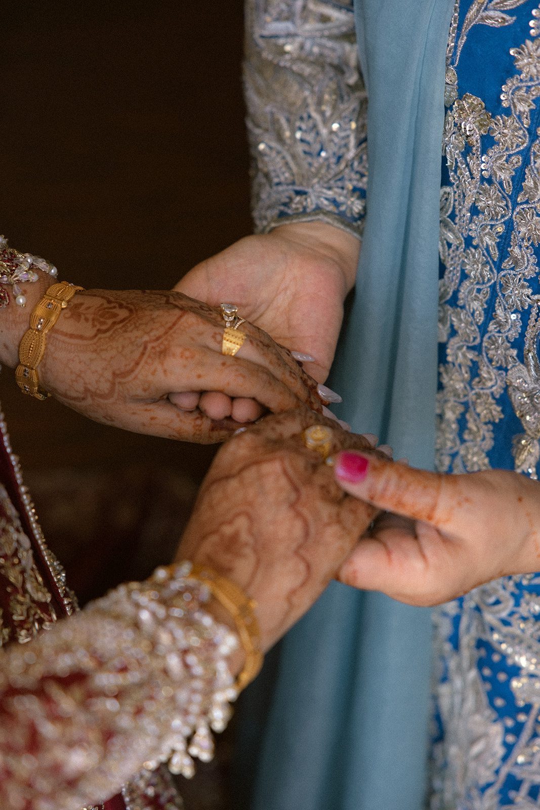 Close-up of henna-decorated hands and gold jewelry during an indian wedding ceremony.