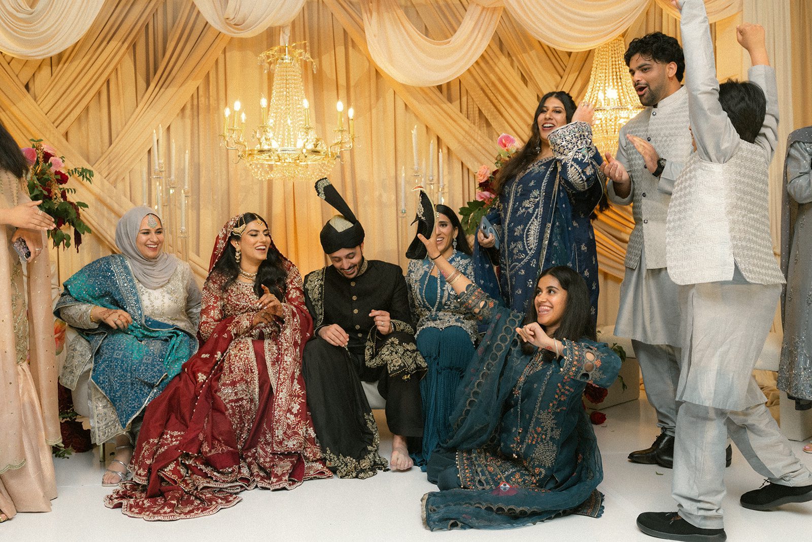 Bride and groom seated with family and friends during a lively indian wedding celebration.