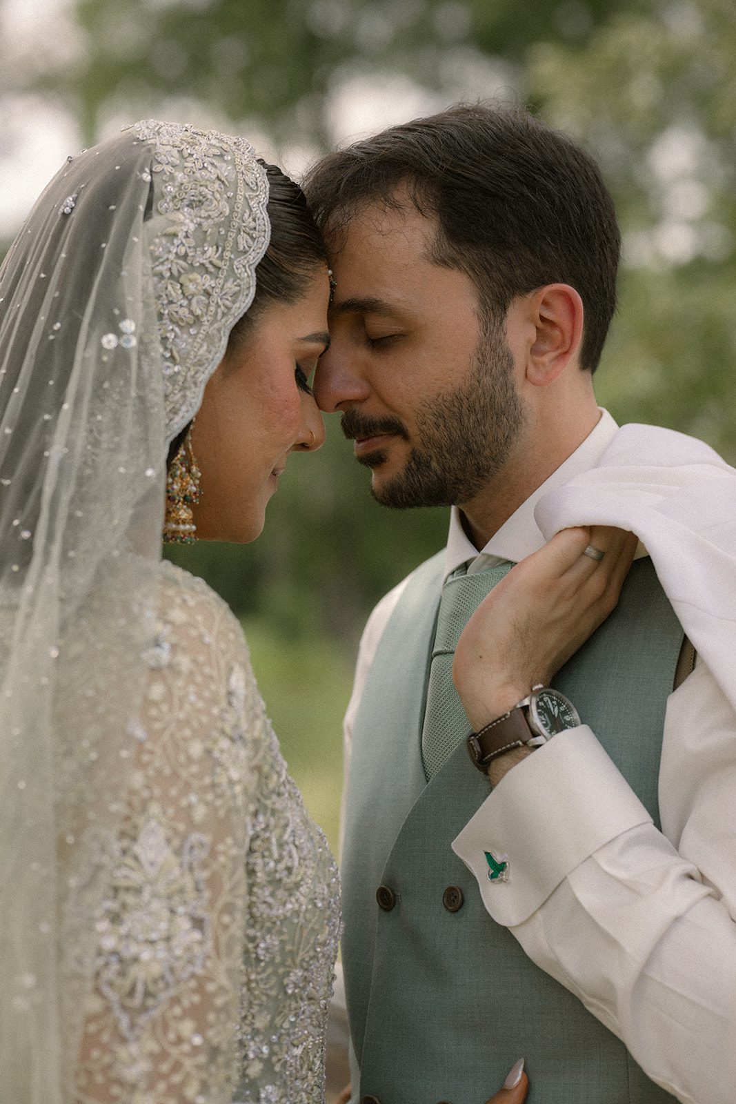 Close-up portrait of a bride and groom touching foreheads in embroidered formal attire during a south asian wedding.