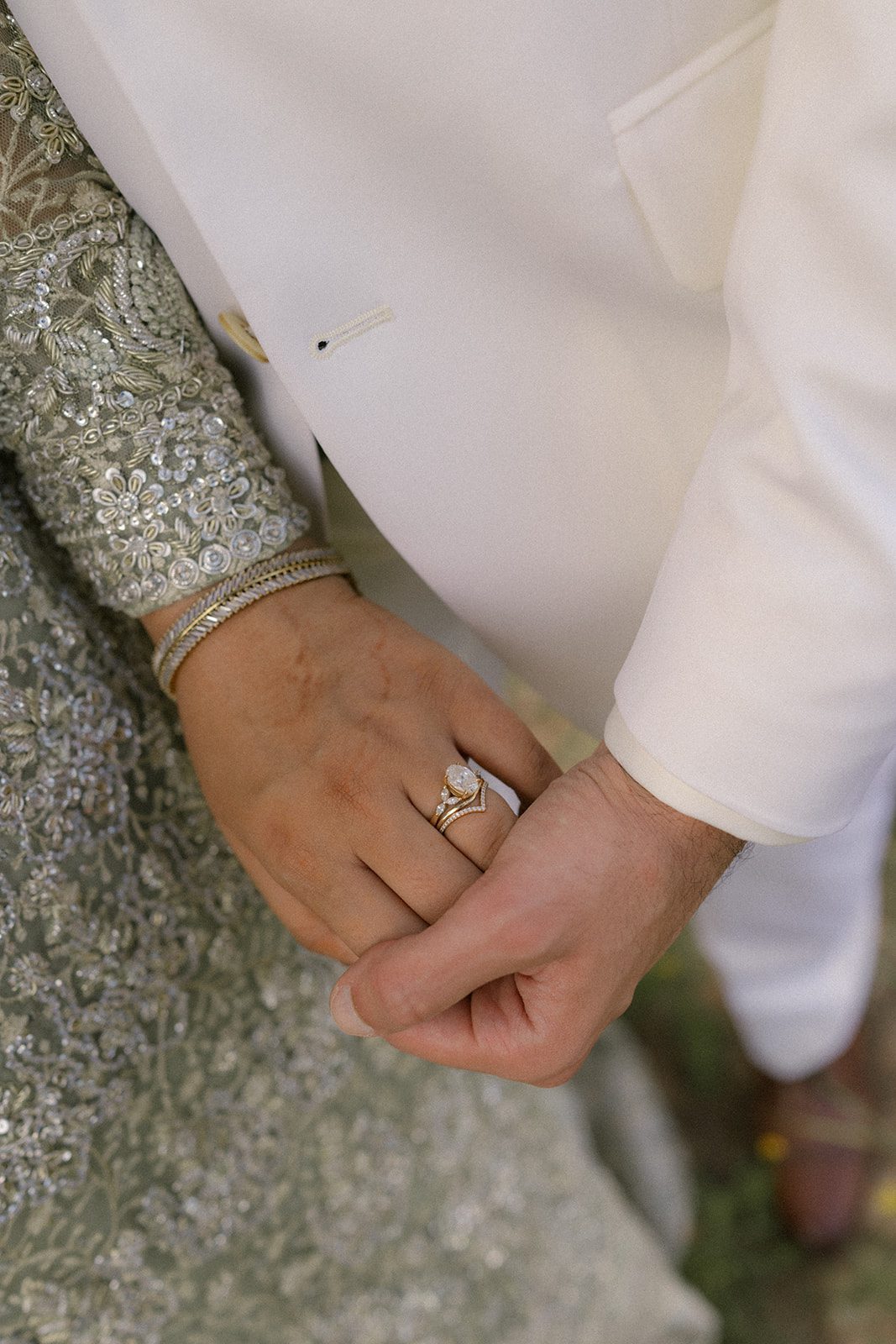 Close-up of the bride and groom holding hands, highlighting her engagement and wedding rings during a multi day wedding celebration.