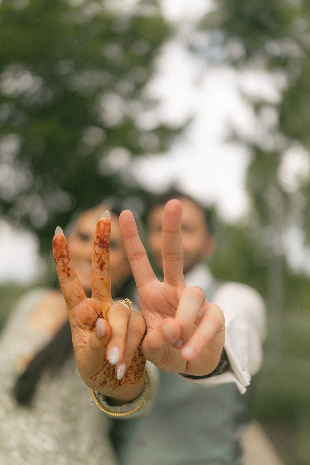 Close-up of the couple making matching hand gestures, highlighting the bride’s mehndi and engagement ring during their indian wedding celebration.