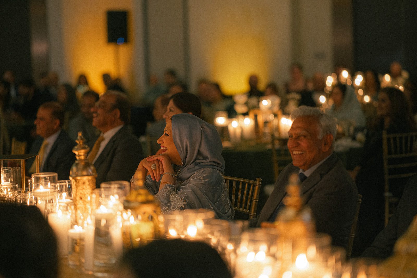 Guests seated at candlelit reception tables laughing together during a multi day wedding, surrounded by warm lantern decor and elegant table settings.