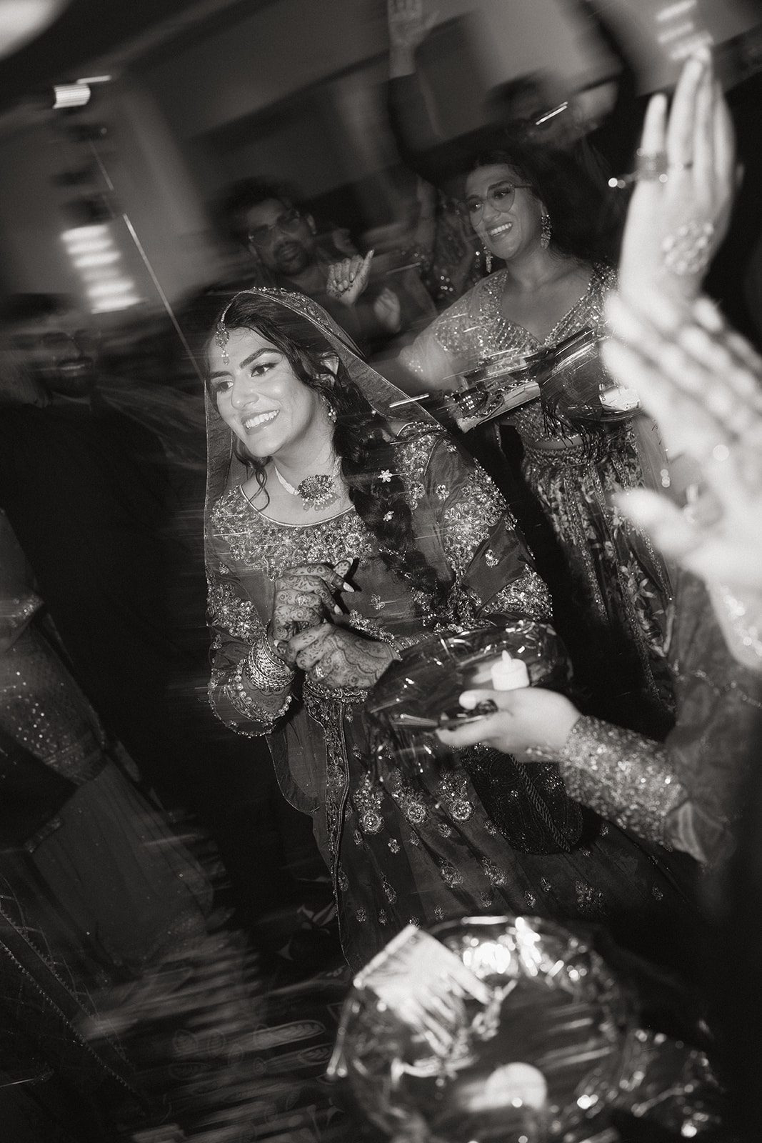 Black-and-white candid of the bride smiling among guests, with intricate mehndi and embroidered attire captured by an indian wedding photographer during the festivities.