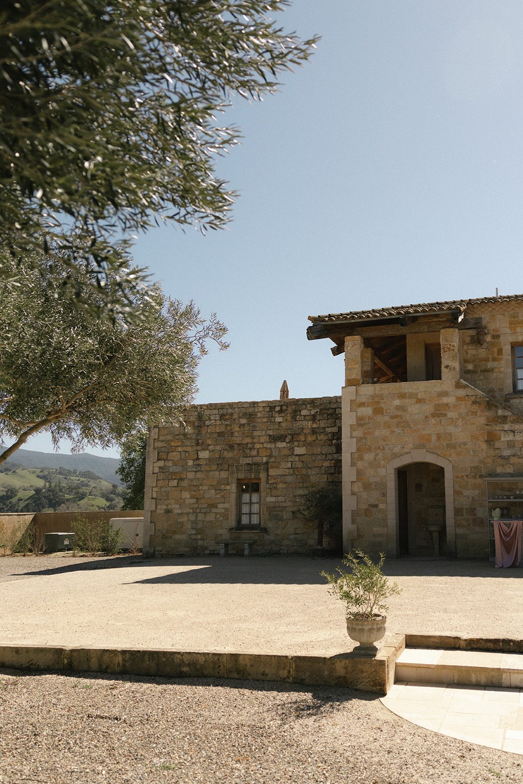 Sunstone Villa wedding venue in Santa Ynez, California, featuring rustic limestone architecture, terracotta roof tiles, olive trees, and a sunlit courtyard overlooking the rolling hills of the Santa Ynez Valley.
