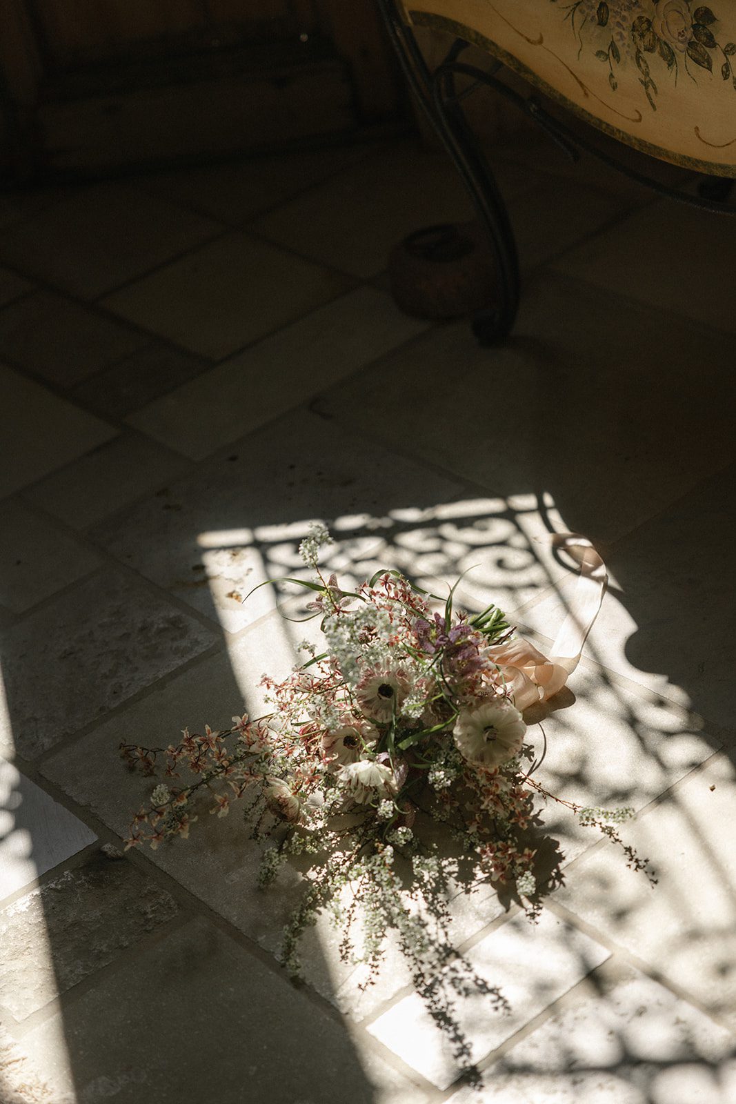 Organic bridal bouquet featuring delicate white blooms, blush pink flowers, and trailing greenery resting on sunlit stone floors during a Sunstone Villa Wedding in California.