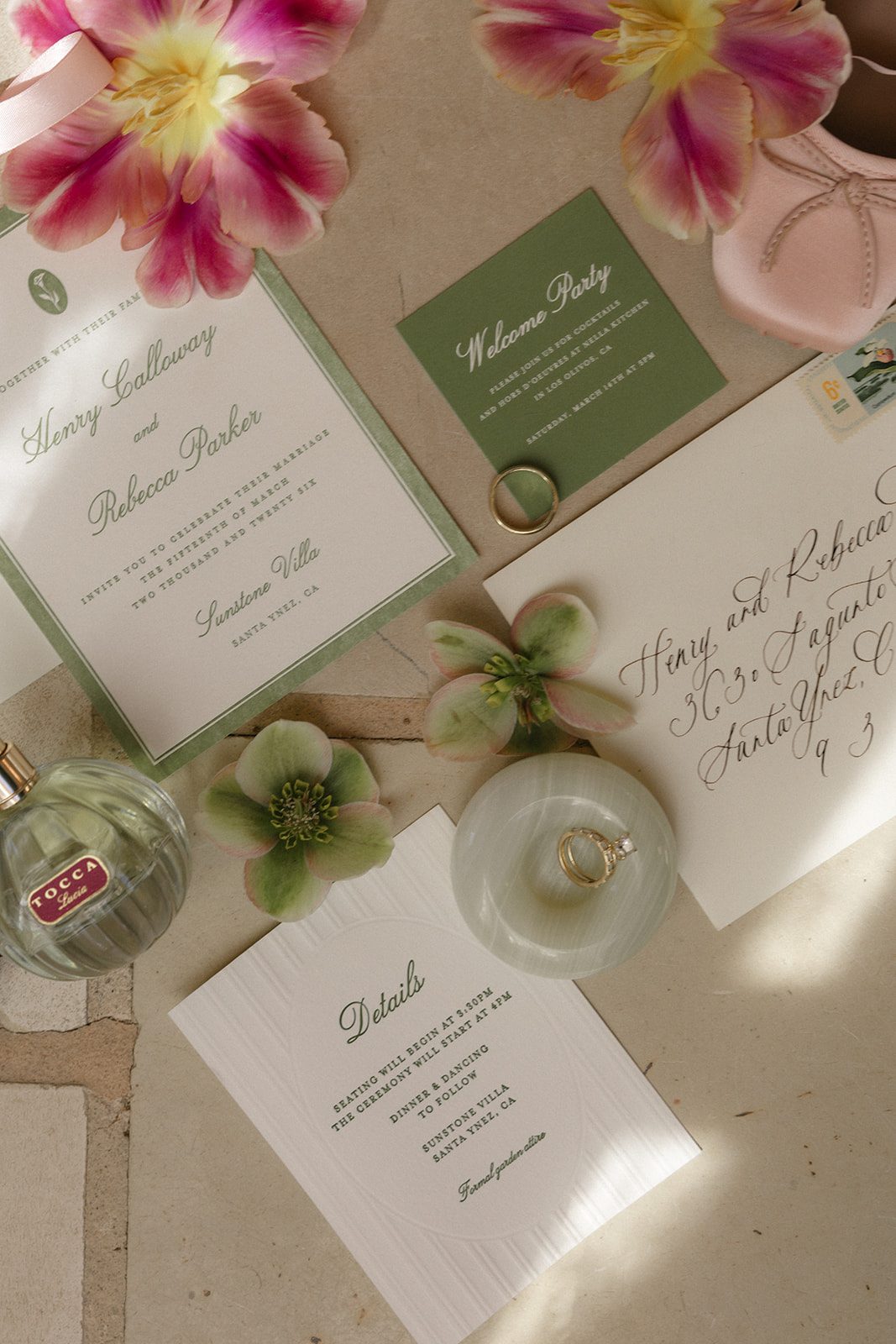 Elegant wedding invitation flat lay for a Sunstone Villa wedding in Santa Ynez, featuring sage green and ivory stationery, handwritten calligraphy, colorful pink tulips, wedding rings, vintage perfume, and delicate bridal accessories.