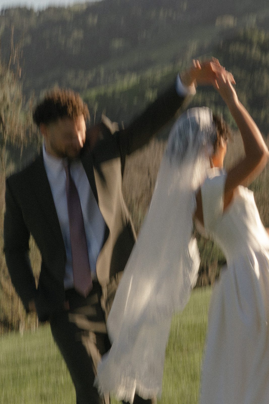 Artistic motion-blurred wedding photograph of a bride and groom twirling together in the golden California sunlight, featuring a flowing lace veil, ivory wedding dress, and dark suit against the vineyards of Santa Ynez Valley.