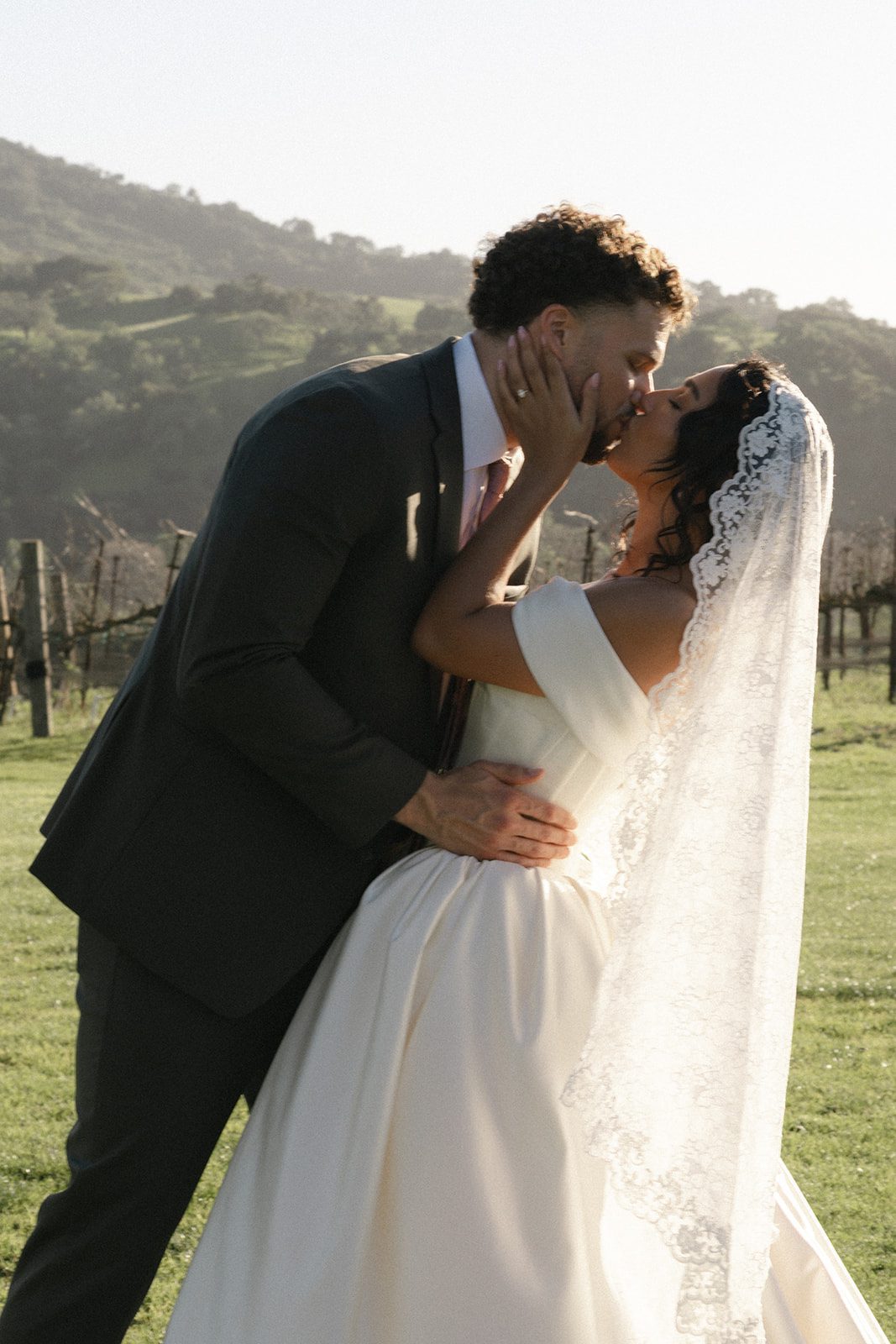 Bride and groom sharing a kiss in golden afternoon light beside the vineyards at Sunstone Villa, a Santa Ynez wedding venue surrounded by rolling California hills.