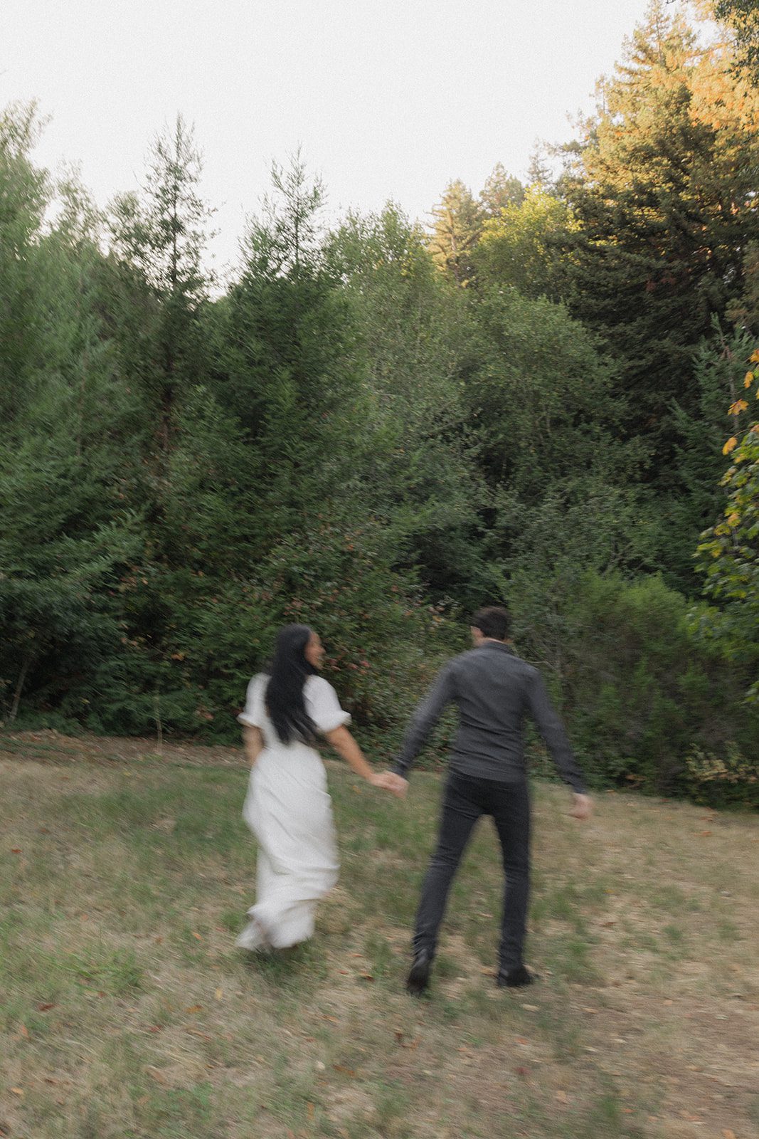 Couple holding hands as they walk toward a wooded trail, candid forest engagement photos highlighting one of the natural engagement photo locations in the Bay Area.