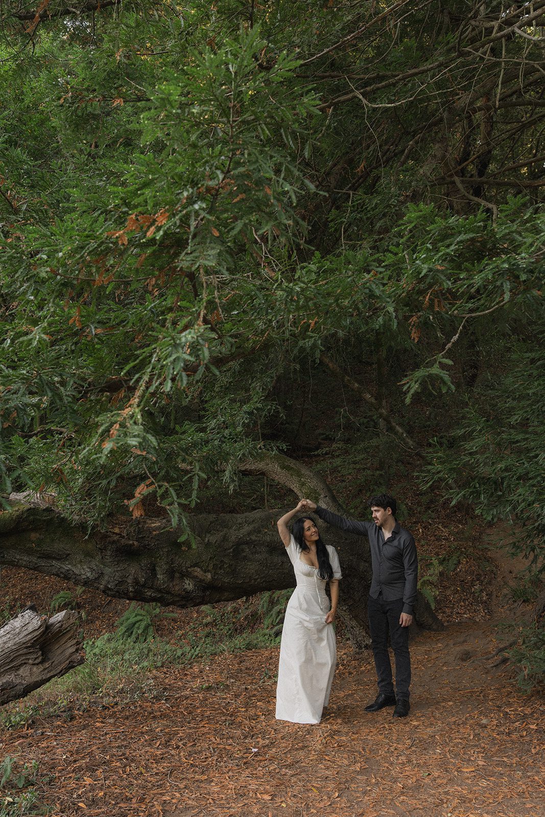Engaged couple dancing beneath dense redwood branches on a woodland trail, captured during Reinhardt Redwood Regional Park Engagement Photos.