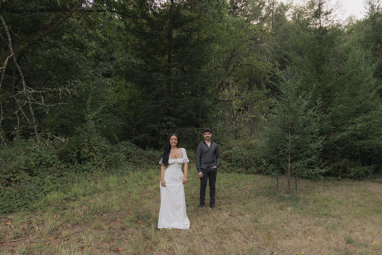Couple standing in a quiet grassy clearing surrounded by dense woodland, showcasing one of the natural engagement photo locations in the Bay Area.