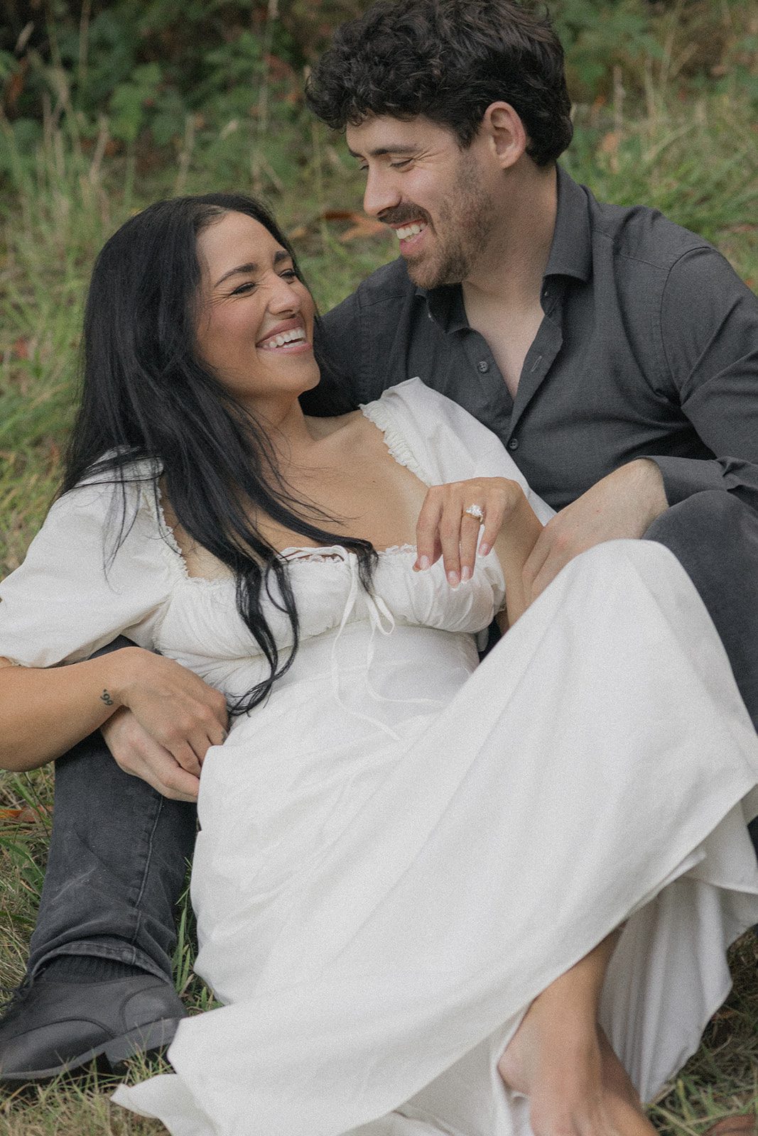 Couple sitting together in a grassy clearing with an engagement ring visible, highlighting natural engagement photo locations in the Bay Area.