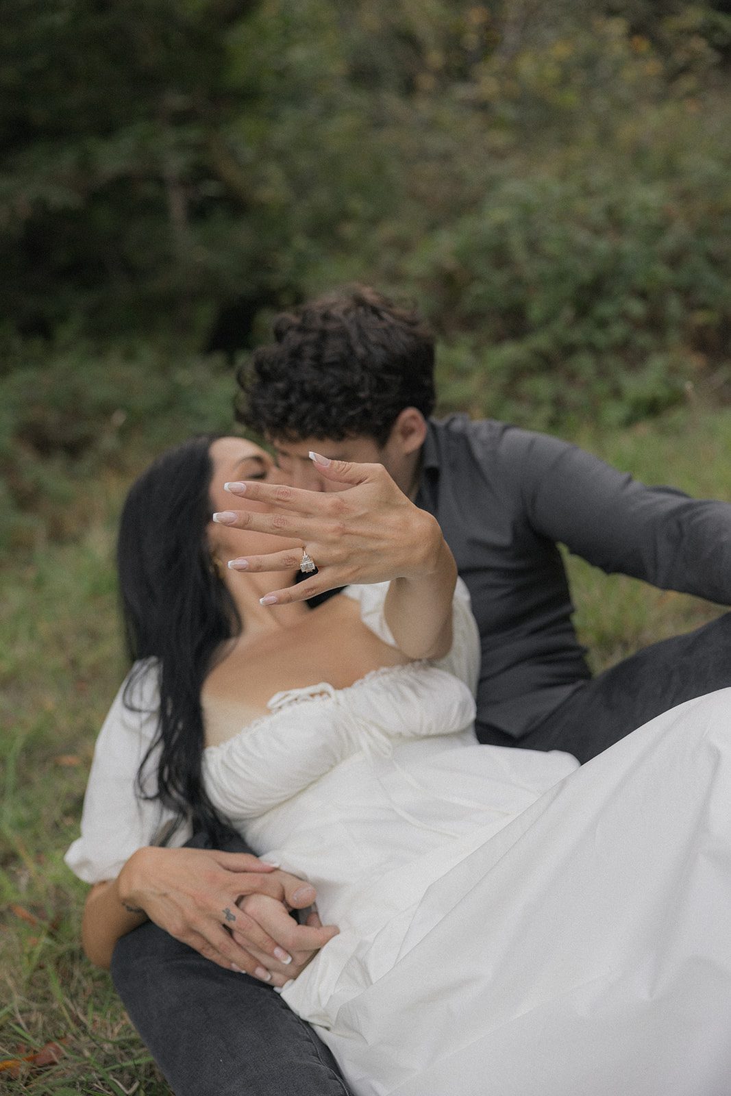 Couple kissing while displaying an engagement ring during a forest session with a Bay Area wedding photographer.