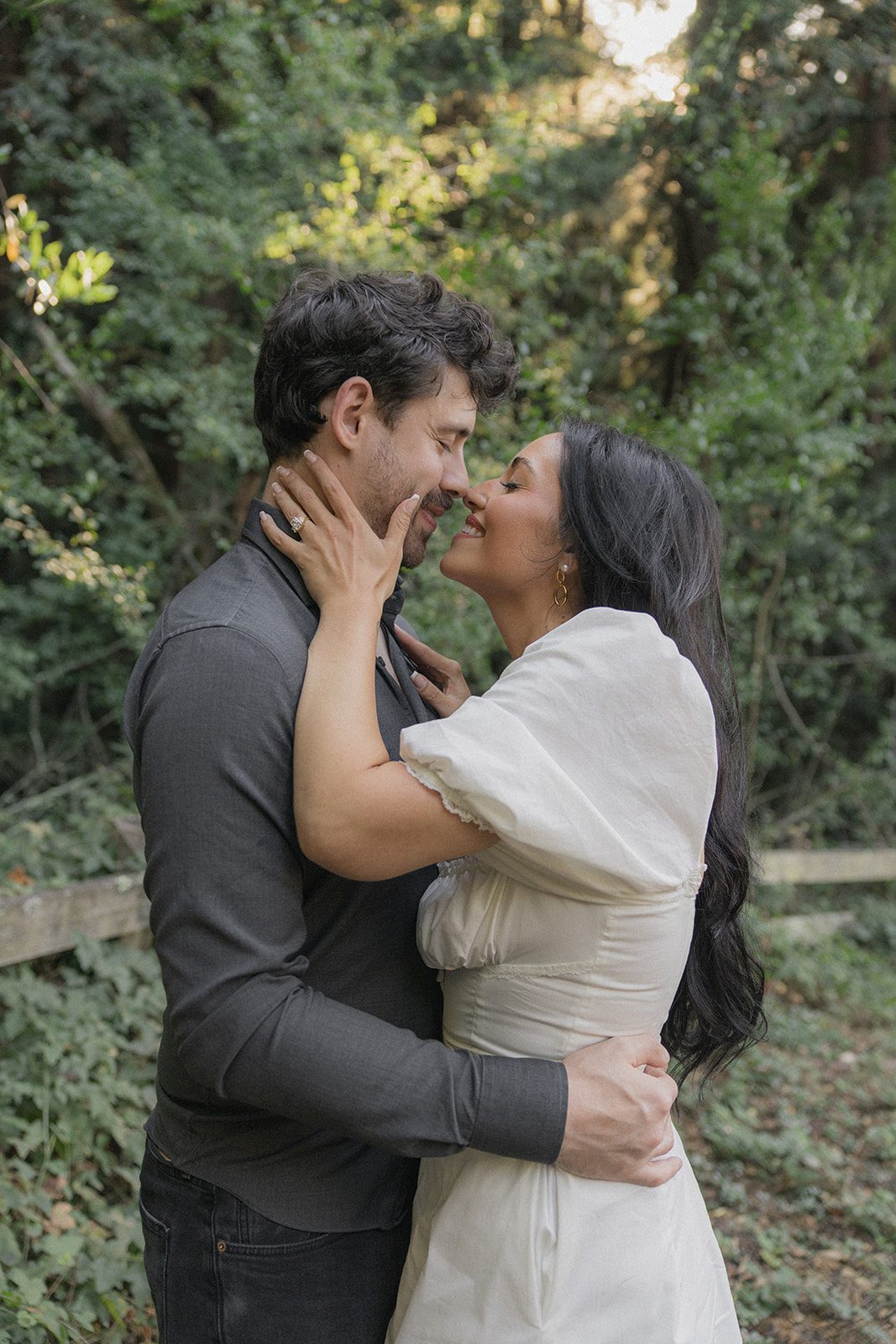 Engaged couple embracing on a sunlit forest trail, with the engagement ring visible in intimate forest engagement photos by a Bay Area wedding photographer.
