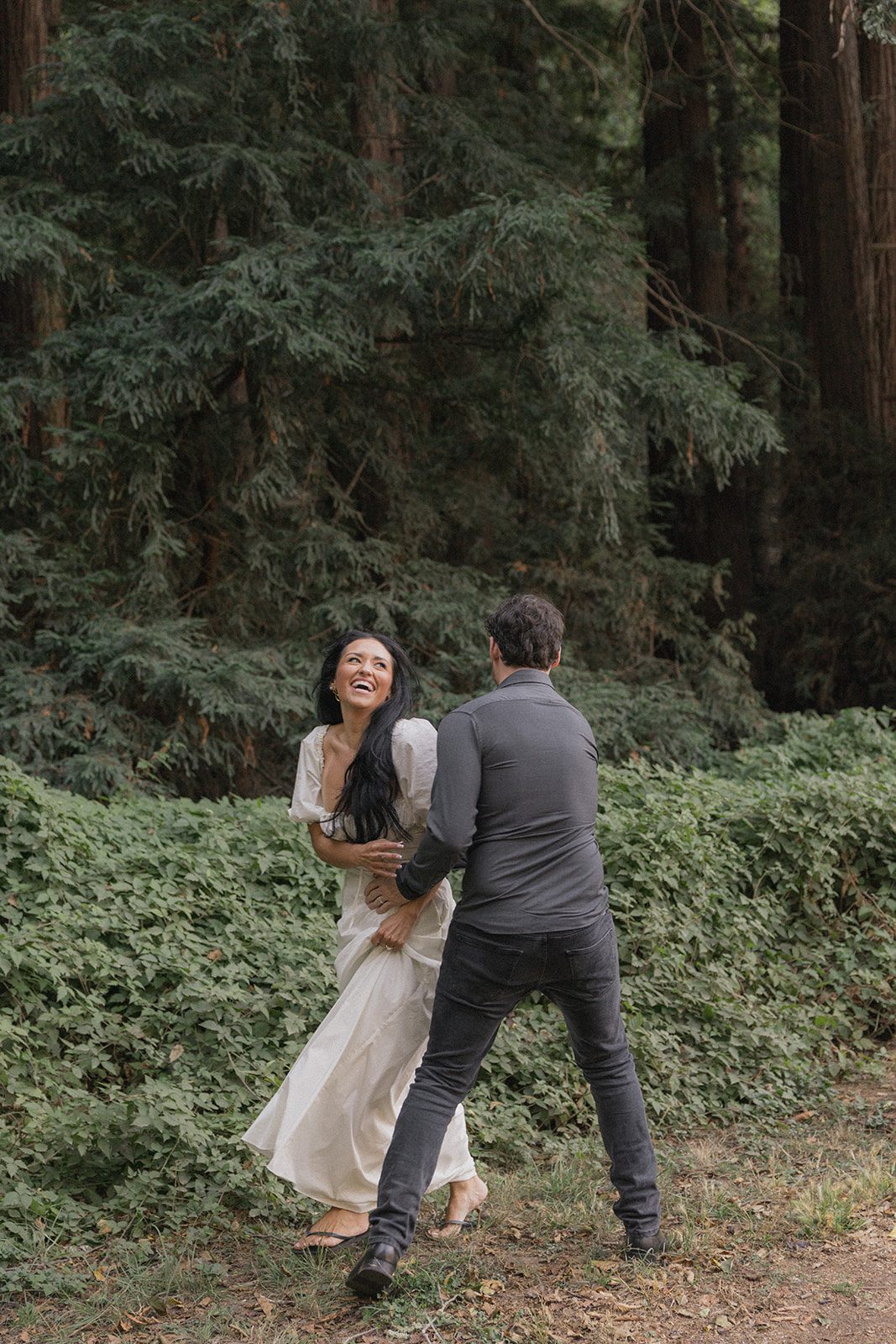 Couple laughing together beside dense redwood foliage during Reinhardt Redwood Regional Park Engagement Photos.