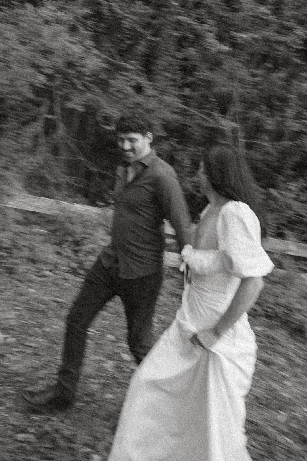 Black-and-white motion portrait of a couple walking together through the woods, an editorial take on forest engagement photos by a Bay Area wedding photographer.