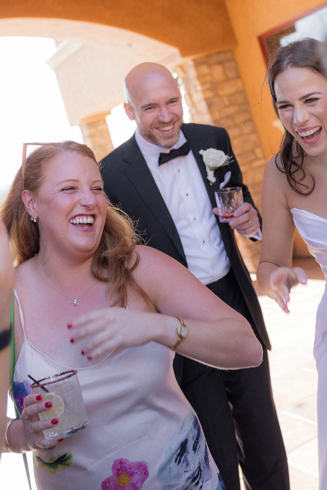Bride and groom laughing with a guest while holding cocktails during their outdoor wedding reception at Villa San Juliette.