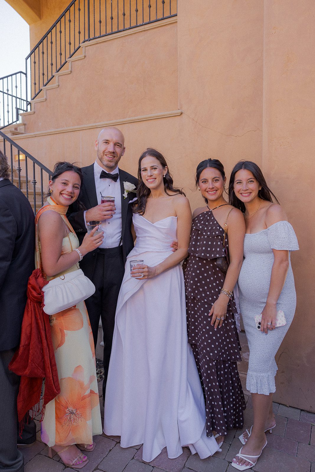 Bride and groom pose with three female guests in colorful formal dresses during an outdoor San Luis Obispo vineyard wedding reception.