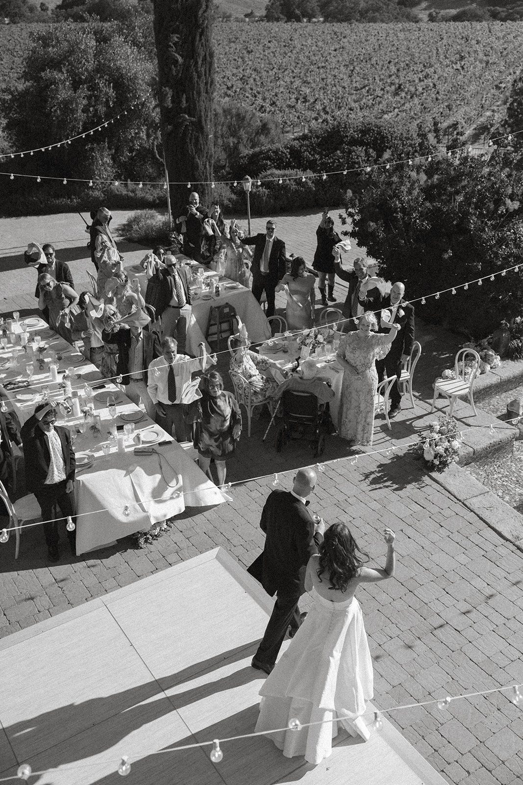 Black-and-white overhead view of newlyweds dancing as guests cheer beneath string lights at a Villa San Juliette wedding reception.