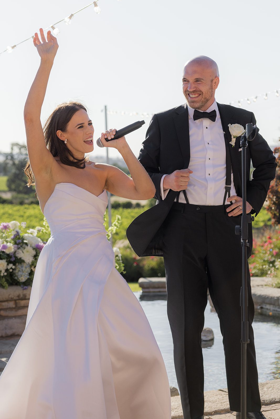 Bride raising her arm while speaking into a microphone beside her smiling groom at their Villa San Juliette wedding reception.