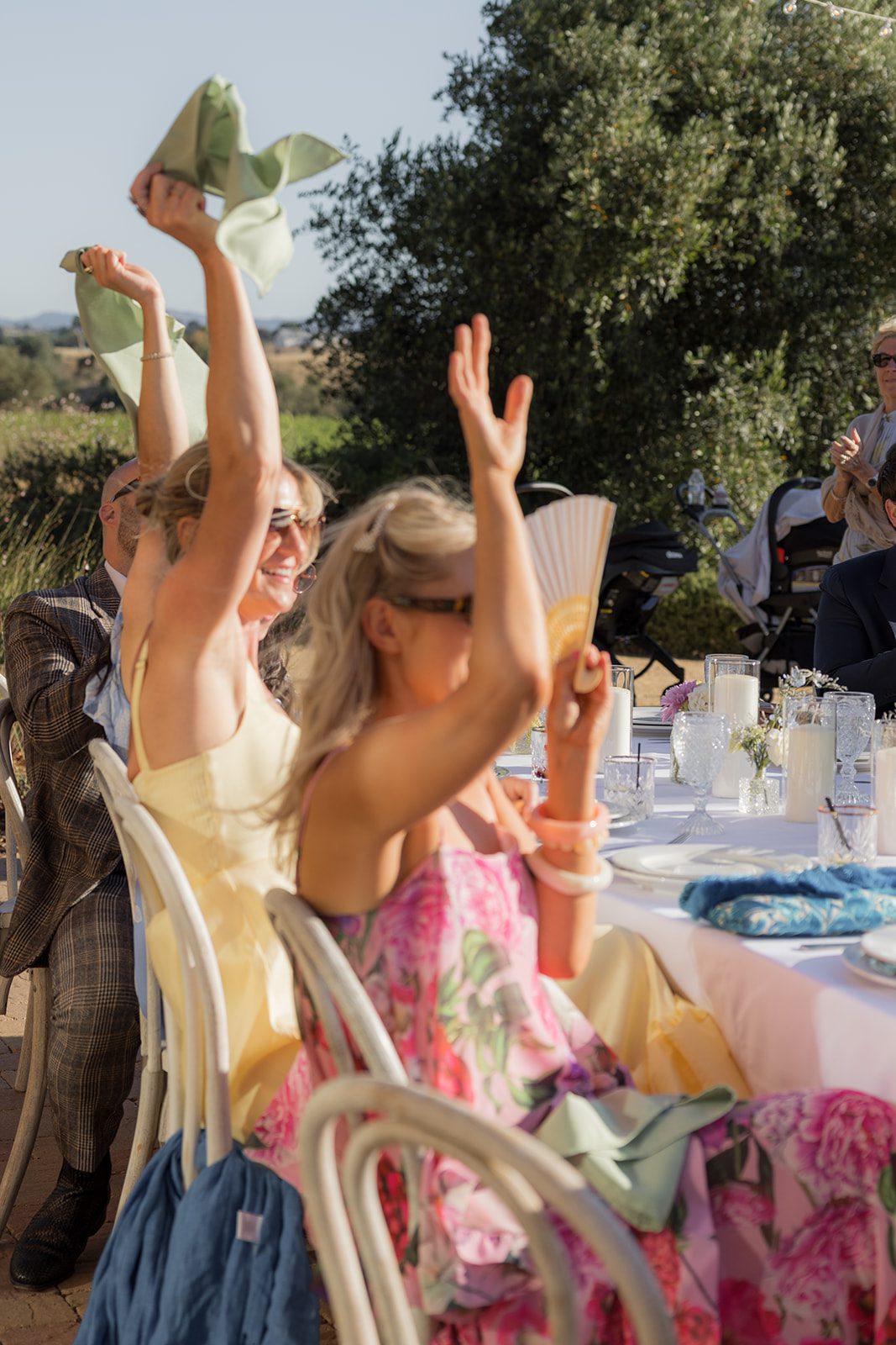 Wedding guests wave green napkins and raise their hands while seated at an outdoor vineyard wedding reception at Villa San Juliette.