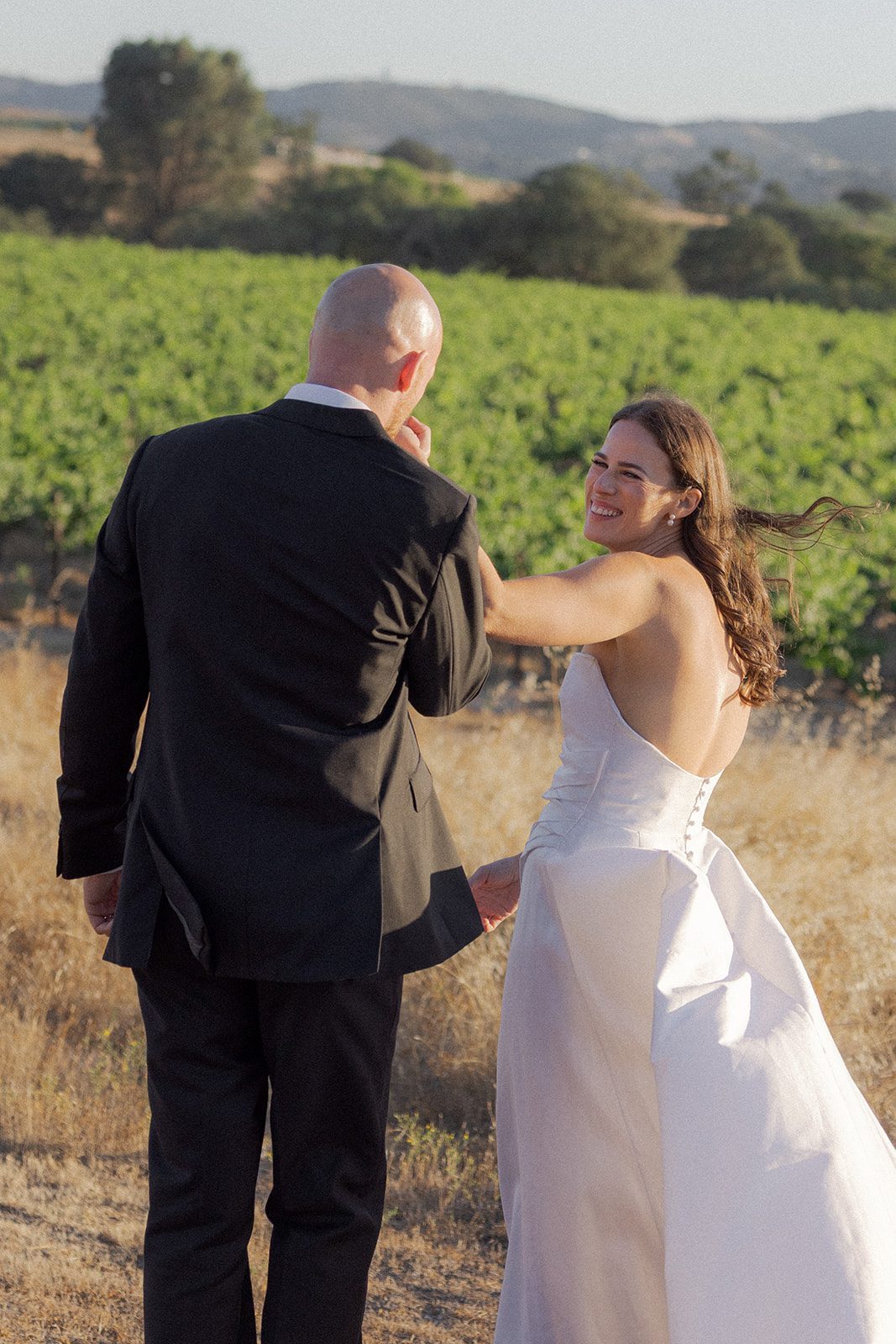 Bride in a strapless white gown smiling at her groom during golden hour portraits at a vineyard wedding venue in California.