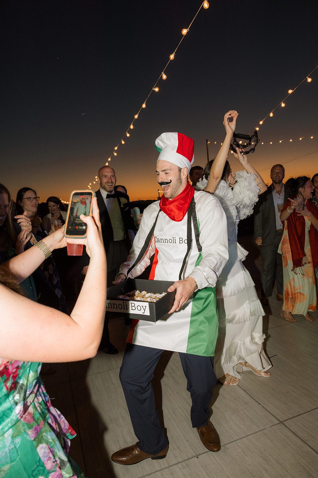 Cannoli server dressed in Italian-themed attire carrying desserts through dancing guests at an outdoor san luis obispo wedding reception.