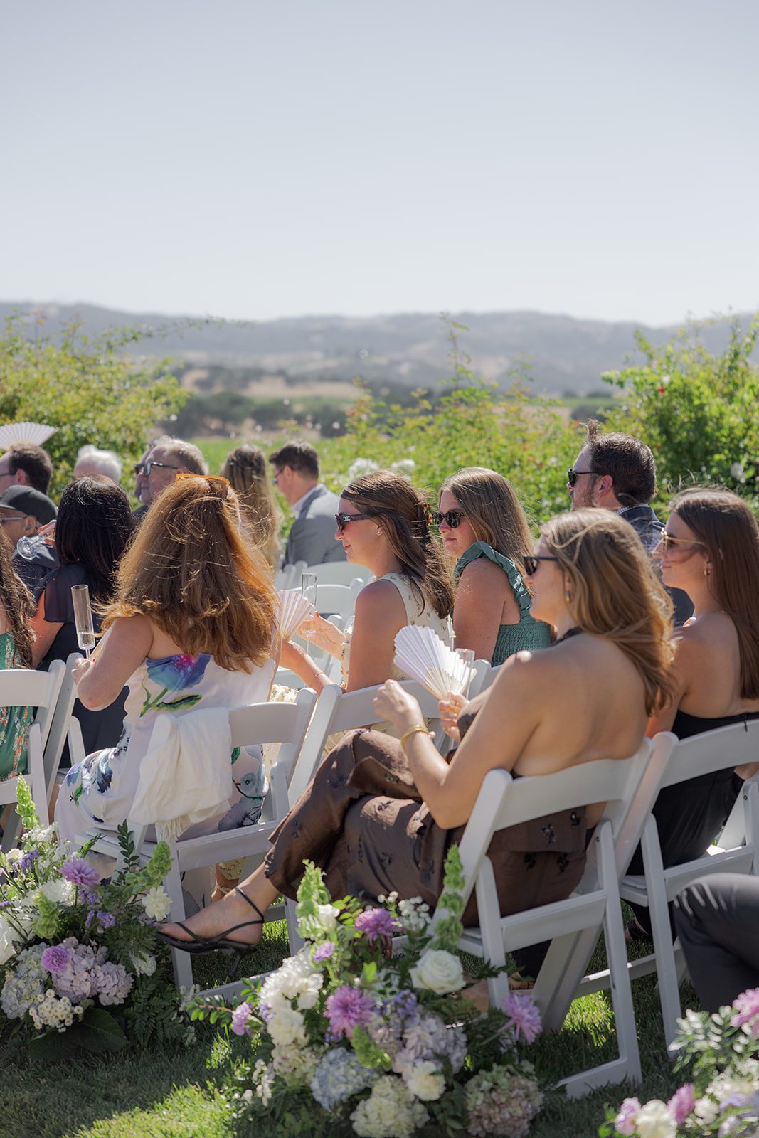 Wedding guests seated among pastel floral arrangements overlooking rolling vineyard hills at a California vineyard wedding venue.