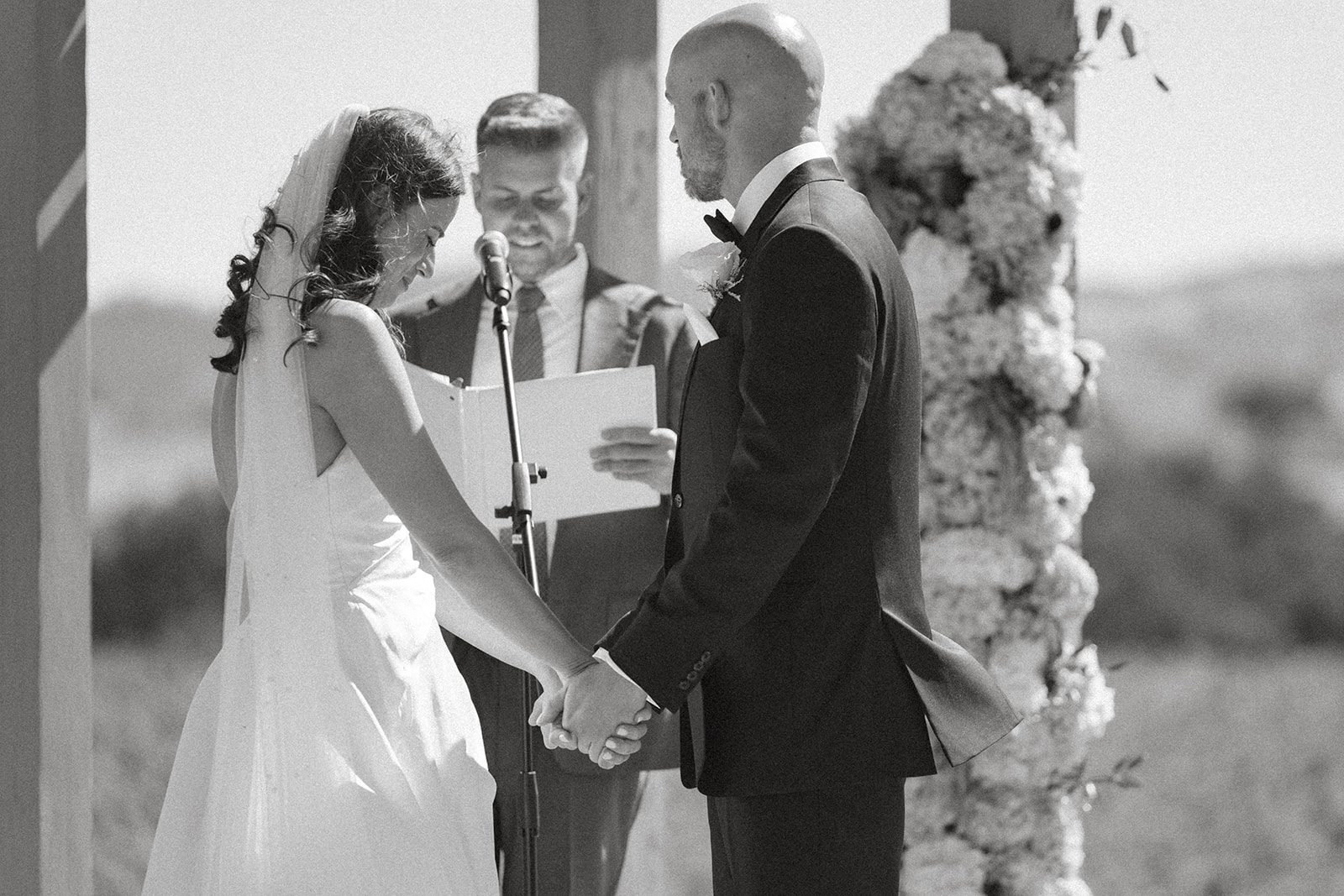 Black-and-white candid of a bride smiling while holding her groom's hands during their san luis obispo wedding ceremony.